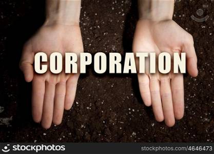 Conceptual word in palms. Male hands on soil background showing in palms idea word corporation