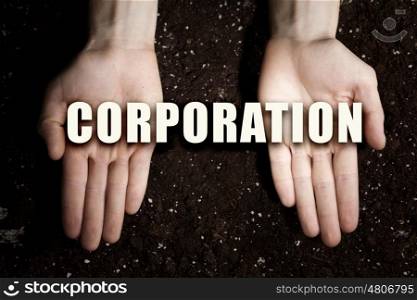 Conceptual word in palms. Male hands on soil background showing in palms idea word corporation