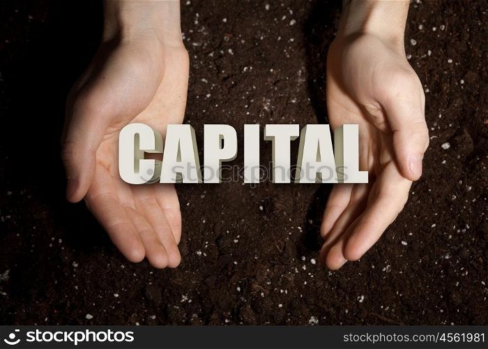 Conceptual word in palms. Male hands on soil background showing in palms word capital