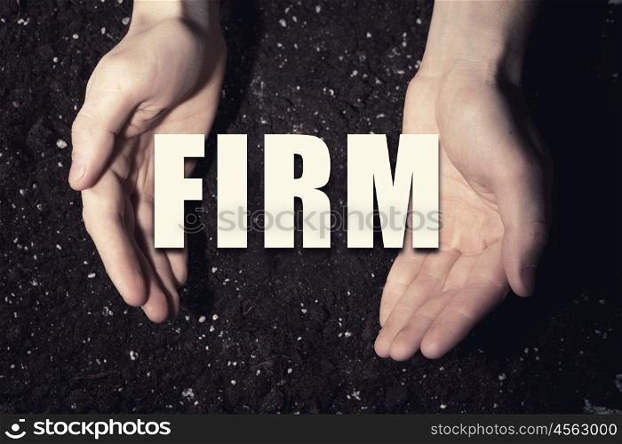 Conceptual word in palms. Male hands on soil background showing in palms word firm