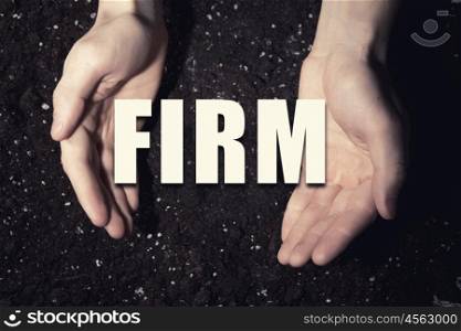Conceptual word in palms. Male hands on soil background showing in palms word firm