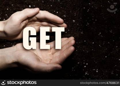 Conceptual word in palms. Male hands on soil background showing in palms word get