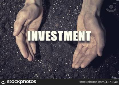 Conceptual word in palms. Male hands on soil background showing in palms word investment