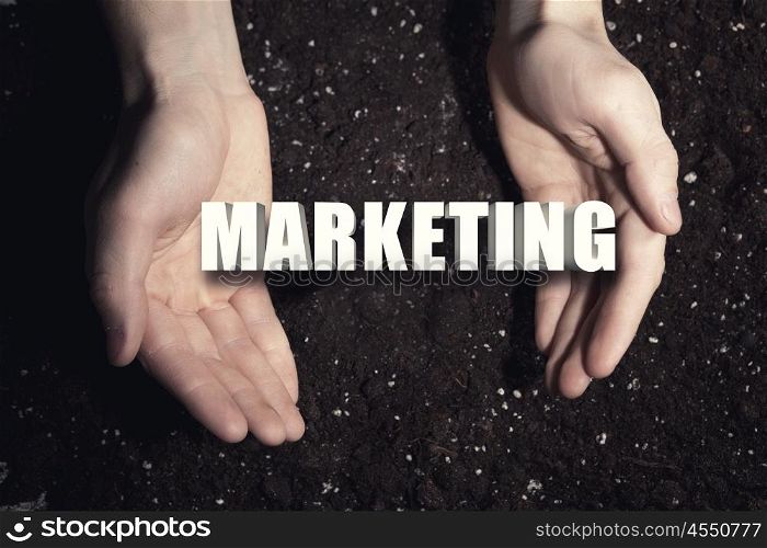 Conceptual word in palms. Male hands on soil background showing in palms word marketing