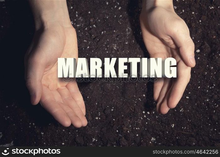 Conceptual word in palms. Male hands on soil background showing in palms word marketing