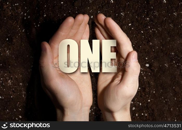 Conceptual word in palms. Male hands on soil background showing in palms word one