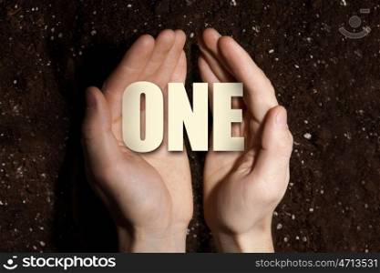 Conceptual word in palms. Male hands on soil background showing in palms word one