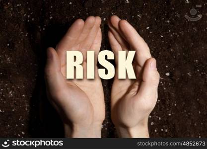 Conceptual word in palms. Male hands on soil background showing in palms word risk