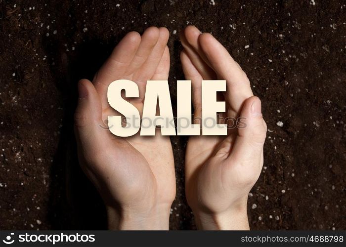 Conceptual word in palms. Male hands on soil background showing in palms word sale