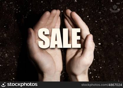 Conceptual word in palms. Male hands on soil background showing in palms word sale
