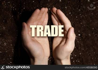 Conceptual word in palms. Male hands on soil background showing in palms word trade