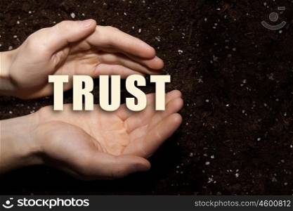 Conceptual word in palms. Male hands on soil background showing in palms word trust
