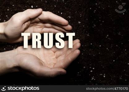 Conceptual word in palms. Male hands on soil background showing in palms word trust