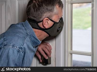 Concerned and worried man wearing a protective breathing mask against flu and coronavirus and looking out of front door. Worried senior caucasian man wearing protective mask against corona virus