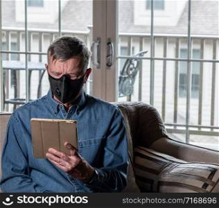 Concerned and worried man wearing a protective breathing mask against flu and coronavirus and reading news on tablet. Worried senior caucasian man wearing protective mask against corona virus