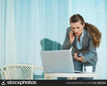 Concerned business woman speaking mobile and looking in laptop