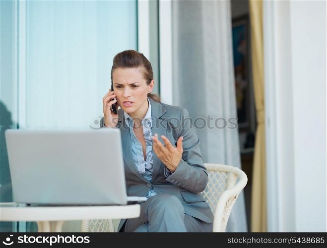 Concerned business woman talking cell phone on terrace