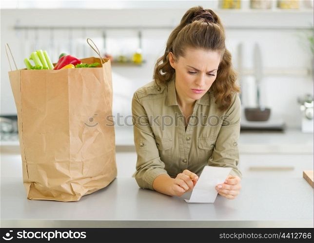 Concerned housewife checking bill after shopping in kitchen