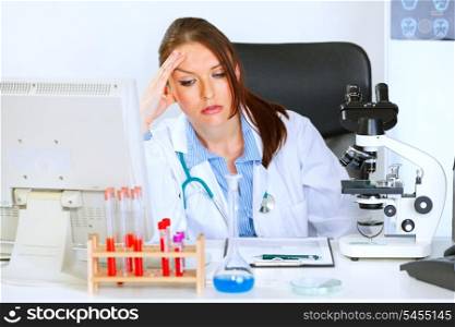 Concerned medical doctor woman sitting at office table and holding hand near head&#xA;