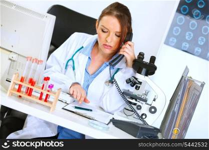 Concerned medical doctor woman talking on phone and looking in clipboard&#xA;