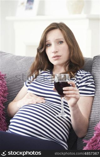 Concerned Pregnant Woman At Home Drinking Glass Of Red Wine