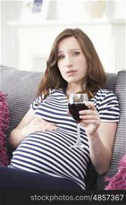 Concerned Pregnant Woman At Home Drinking Glass Of Red Wine
