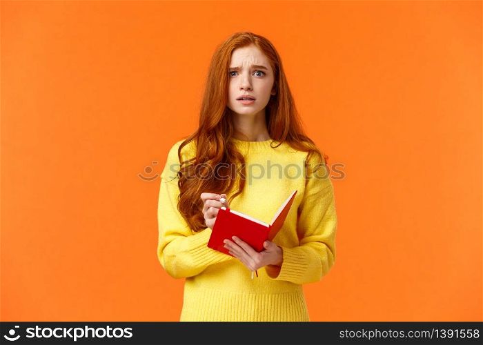 Concerned tensed attractive redhead female student cant write down everything from blackboard after lector, biting lip look troubled and perplexed, holding red notebook and pen, orange background.. Concerned tensed attractive redhead female student cant write down everything from blackboard after lector, biting lip look troubled and perplexed, holding red notebook and pen, orange background