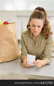 Concerned young housewife examines check after shopping