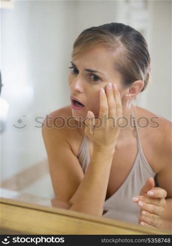Concerned young woman in bathroom checking skin condition