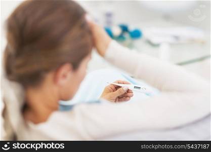 Concerned young woman looking on thermometer