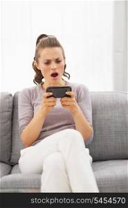 Concerned young woman sitting on sofa and reading sms