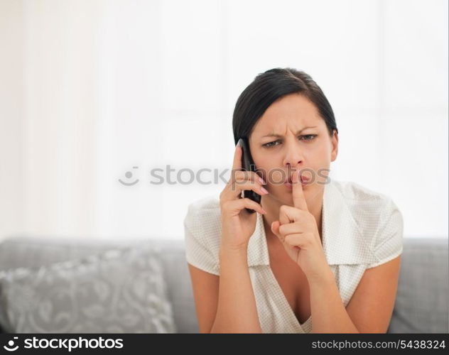 Concerned young woman speaking mobile phone and showing shh gesture