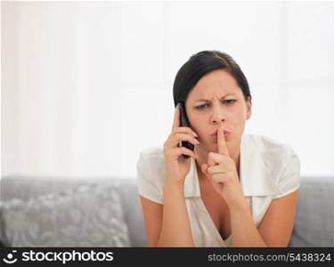 Concerned young woman speaking mobile phone and showing shh gesture