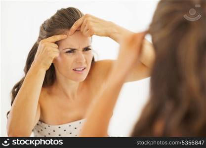 Concerned young woman squeezing acne in bathroom