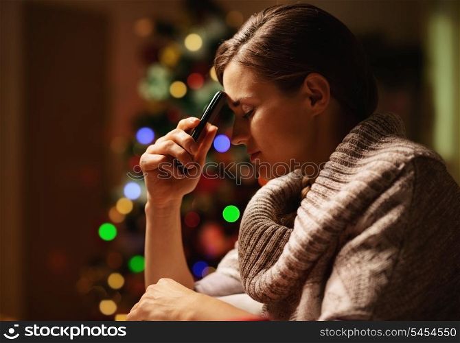 Concerned young woman with mobile phone in front of christmas tree