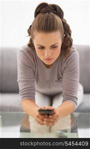 Concerned young woman witn cell phone in hands sitting on couch