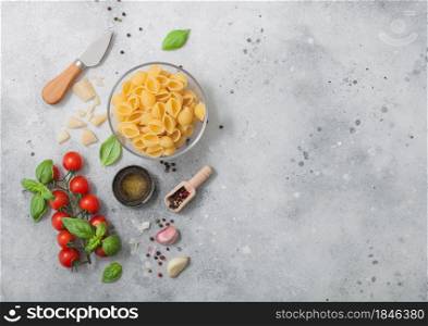 Conchiglie pasta in glass bowl with parmesan cheese and tomatoes, oil and garlic with basil on light background. Space for text