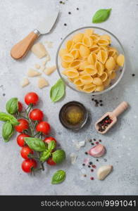 Conchiglie pasta in glass bowl with parmesan cheese and tomatoes, oil and garlic with basil on light background. Top view