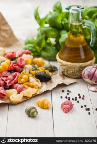 Conchiglioni raw tricolore pasta in brown paper on light wooden background with basil and oil.