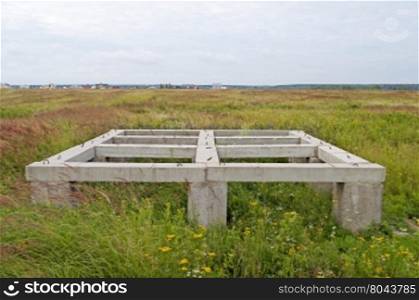 Concrete pier foundation of small country house in the meadow on summer