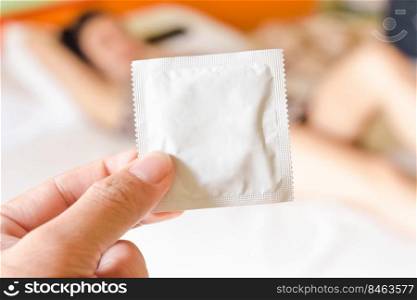 Condom package in a hand against a blurred female background on the white bed