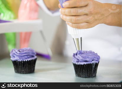 Confectioner decorate some cupcakes with pastry bag