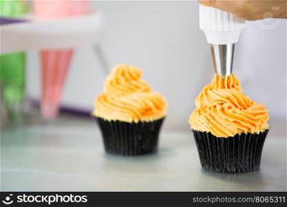 Confectioner decorate some cupcakes with pastry bag