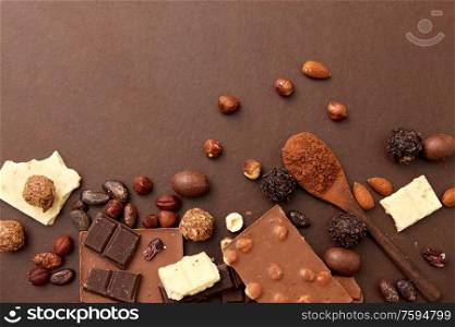 confectionery and food concept - milk, dark and white chocolate bars with nuts, candies, cocoa beans and powder on brown background. chocolate with nuts, cocoa beans and powder