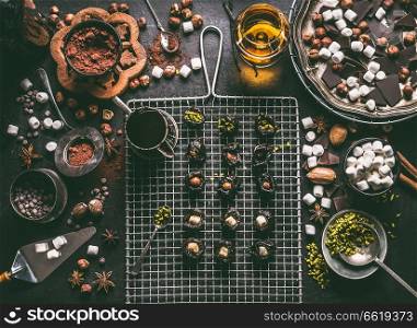 Confectionery or patisserie concept. Preparation of pralines with prunes soaked in rum and stuffed with nuts, marshmallow and pistachio on dark table background with chocolate and ingredients