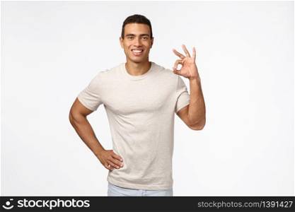 Confident and pleased young hispanic man in good shape, showing okay, approval or good sign and smiling in agreement, give positive feedback, recommend product, white background. Copy space. Confident and pleased young hispanic man in good shape, showing okay, approval or good sign and smiling in agreement, give positive feedback, recommend product, white background