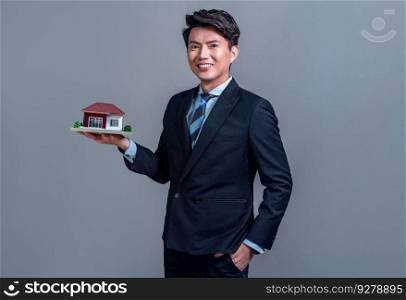 Confident Asian businessman holding house model, advertising home loan with smile. Real estate agent with s&le house model in hand on isolated background for housing business advertisement. Jubilant. Confident Asian businessman holding house model. Jubilant