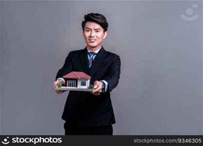 Confident Asian businessman holding house model, advertising home loan with smile. Real estate agent with s&le house model in hand on isolated background for housing business advertisement. Jubilant. Confident Asian businessman holding house model. Jubilant