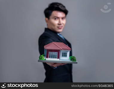 Confident Asian businessman holding house model, advertising home loan with smile. Real estate agent with sample house model in hand on isolated background for housing business advertisement. Jubilant. Confident Asian businessman holding house model. Jubilant