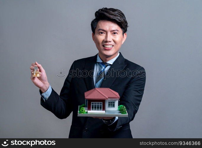 Confident Asian businessman holding house model, advertising home loan with smile. Real estate agent with sample house model in hand on isolated background for housing business advertisement. Jubilant. Confident Asian businessman holding house model. Jubilant